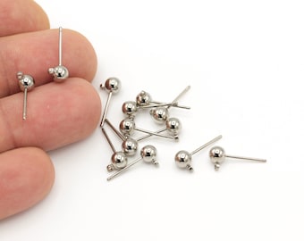 May include: A collection of silver-colored stud earring posts with small, round, shiny ball accents. The posts are thin and straight, with a small loop at the end of the post. The earrings are scattered on a white surface.