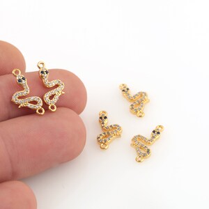 Pode incluir: Cinco pingentes de cobra de ouro com pedras de zircônia cúbica transparentes e pretas. Cada pingente tem um laço na parte superior para prender a uma corrente ou pulseira.