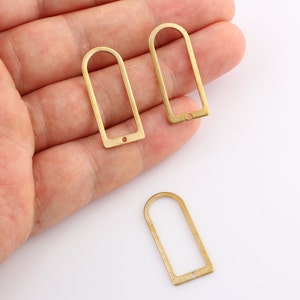 Könnte beinhalten: Drei goldfarbene rechteckige Metallrahmen mit abgerundeten Oberseiten und einem kleinen Loch unten. Die Rahmen liegen auf einer weißen Oberfläche.