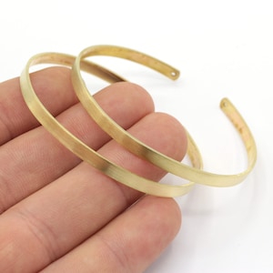 Peut inclure: Deux bracelets en métal couleur or, l'un légèrement plus grand que l'autre, sont empilés l'un sur l'autre. Les bracelets sont simples et ont une finition lisse et brossée.