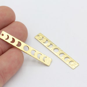 Könnte beinhalten: Zwei goldene Metall-Anhänger mit gehämmerter Textur und einem Design aus Halbmonden in verschiedenen Phasen.