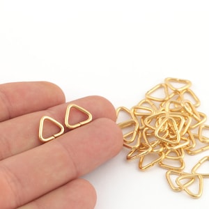 May include: A close-up of a pile of gold-coloured triangle-shaped metal rings. Two of the rings are being held in a hand.
