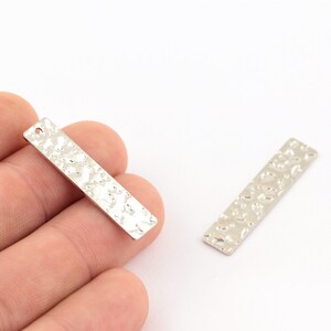 May include: Two silver metal bar pendants with a textured hammered finish. Each pendant has a hole at the top for attaching a chain or string.