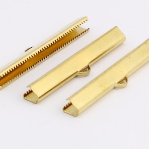 May include: Three gold metal clasps for jewellery making. Each clasp is rectangular with a small loop on one end. One clasp has a serrated edge.