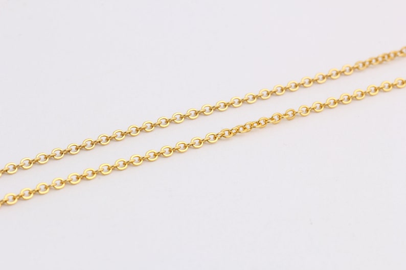 K&ouml;nnte beinhalten: Eine goldene Kettenkette mit einem zarten, kabelartigen Kettenmuster. Die Kette liegt flach auf einer wei&szlig;en Oberfl&auml;che.