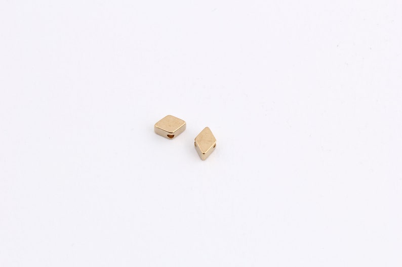 May include: Two gold-colored diamond-shaped beads with a hole in the center.