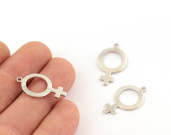 Puede incluir: Abalorios de metal plateado con forma del símbolo de Venus, también conocido como símbolo femenino. Los abalorios tienen una parte superior circular con una cruz debajo y un pequeño lazo para sujetar a la joyería. Se ven tres abalorios.