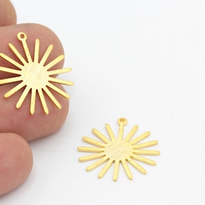 May include: Two gold-colored metal sunburst charms with a hole at the top for hanging. The charms are on a white background.