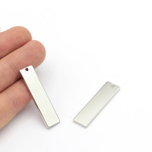 May include: Two silver metal rectangular tags with a hole at the top for hanging. The tags are blank and ready for personalization.
