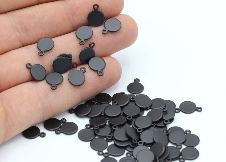 May include: A large quantity of black metal round charms with a loop on top. The charms are scattered on a white surface.
