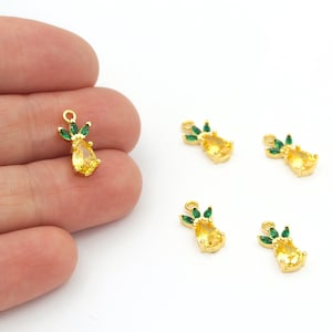 Pode incluir: Cinco pingentes de abacaxi dourados com folhas de cristal verde. Os pingentes são perfeitos para fazer joias ou adicionar um toque de fantasia aos artesanatos.