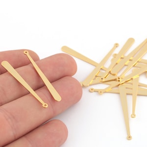 May include: A pile of gold-coloured metal baseball bat charms with a small loop at the top. Two charms are held in a hand.