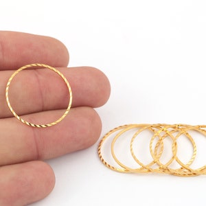 May include: A set of six gold-colored metal rings with a textured, twisted design. The rings are stacked on top of each other.