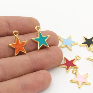 Puede incluir: Surtido de dijes en forma de estrella de tono dorado con pintura de esmalte en varios colores, incluidos rojo, azul, verde, negro, blanco y rosa.