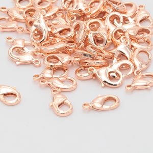 May include: A pile of rose gold lobster clasps, a type of jewelry finding used for making necklaces, bracelets, and other jewelry.