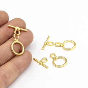 May include: Four gold-toned metal toggle clasps with a round ring and a bar. The clasps are used for jewelry making and crafting.