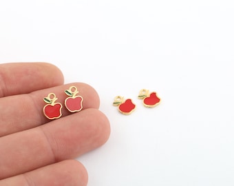May include: Four gold-colored apple charms with red enamel and green leaf accents. The charms are perfect for adding a touch of whimsy to jewelry or crafts.