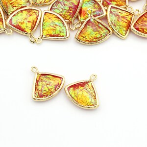 May include: A group of gold-toned metal charms with iridescent red and yellow glass inserts. The charms are shaped like a fan and have a loop at the top for attaching to jewelry.