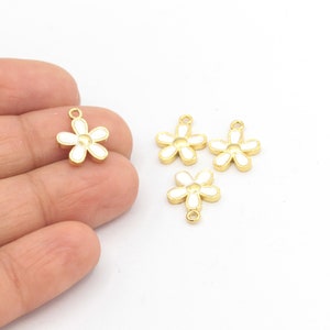 Puede incluir: Cuatro abalorios de flores de tono dorado con esmalte blanco. Cada abalorio tiene un bucle para sujetarlo a joyas.