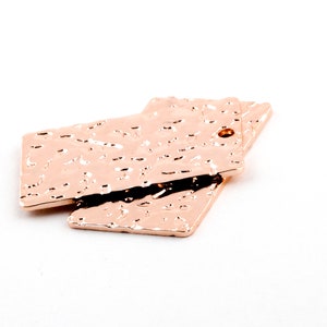 Peut inclure: Deux étiquettes en métal rose gold avec une texture martelée. Les étiquettes sont rectangulaires et ont un trou en haut.