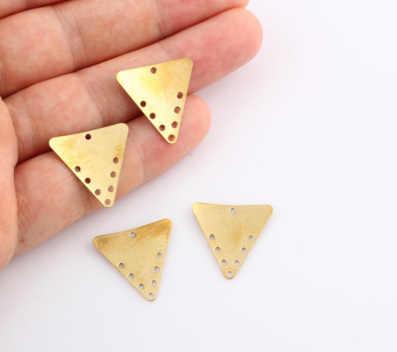 K&ouml;nnte beinhalten: Vier goldfarbene dreieckige Metallanh&auml;nger mit kleinen L&ouml;chern an den R&auml;ndern. Die Anh&auml;nger haben eine geb&uuml;rstete Oberfl&auml;che.