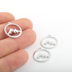 May include: Three silver metal charms in the shape of a circle with a mountain range silhouette inside.