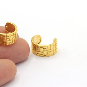 May include: A pair of gold-tone ear cuffs with a geometric pattern. The cuffs are made of metal and have a smooth finish.