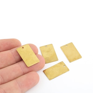 Può includere: Quattro etichette rettangolari in metallo dorato con un piccolo foro nella parte superiore. Le etichette sono su una superficie bianca.
