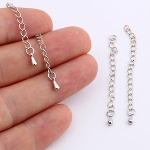 Puede incluir: Dos cadenas de extensión plateadas con una cuenta en forma de lágrima al final de cada cadena.