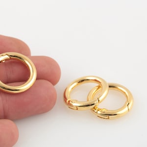 Puede incluir: Tres llaveros de metal de color dorado con cierre de resorte. Los llaveros se muestran sobre una superficie blanca.