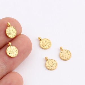 Può includere: Cinque ciondoli in metallo color oro a forma di moneta con un design intricato. I ciondoli hanno un anello nella parte superiore per essere attaccati a gioielli o altri oggetti artigianali.