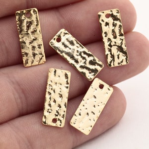 May include: Five gold-coloured metal rectangular tags with a hammered texture and a small hole at the top.