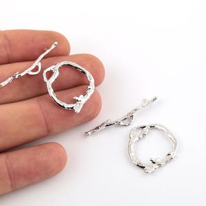 May include: Four silver metal jewelry findings in the shape of a twig. Two of the findings are open circles and two are straight pieces.