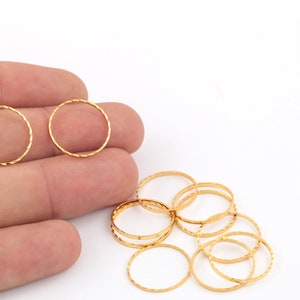 May include: A set of ten gold-colored metal jump rings. The rings are round and have a textured surface. The rings are arranged in a pile on a white surface.