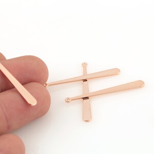 May include: Four rose gold coloured metal pieces shaped like baseball bats with a small loop at the top.