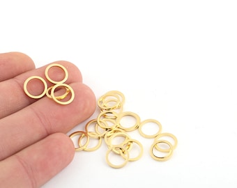 May include: A pile of gold-colored jump rings, a type of jewelry finding, are scattered on a white surface. Some of the rings are held in a hand.