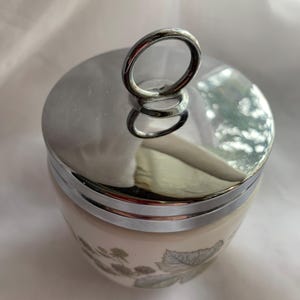 K&ouml;nnte beinhalten: Eine wei&szlig;e Keramik-Eierbecher mit Blumenmuster und einem silbernen Deckel mit einem Ringgriff.