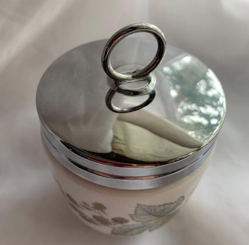 K&ouml;nnte beinhalten: Eine wei&szlig;e Keramik-Eierbecher mit Blumenmuster und einem silbernen Deckel mit einem Ringgriff.