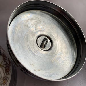 K&ouml;nnte beinhalten: Nahaufnahme der Unterseite eines silbernen Deckels mit einer kleinen Metallschlaufe in der Mitte.
