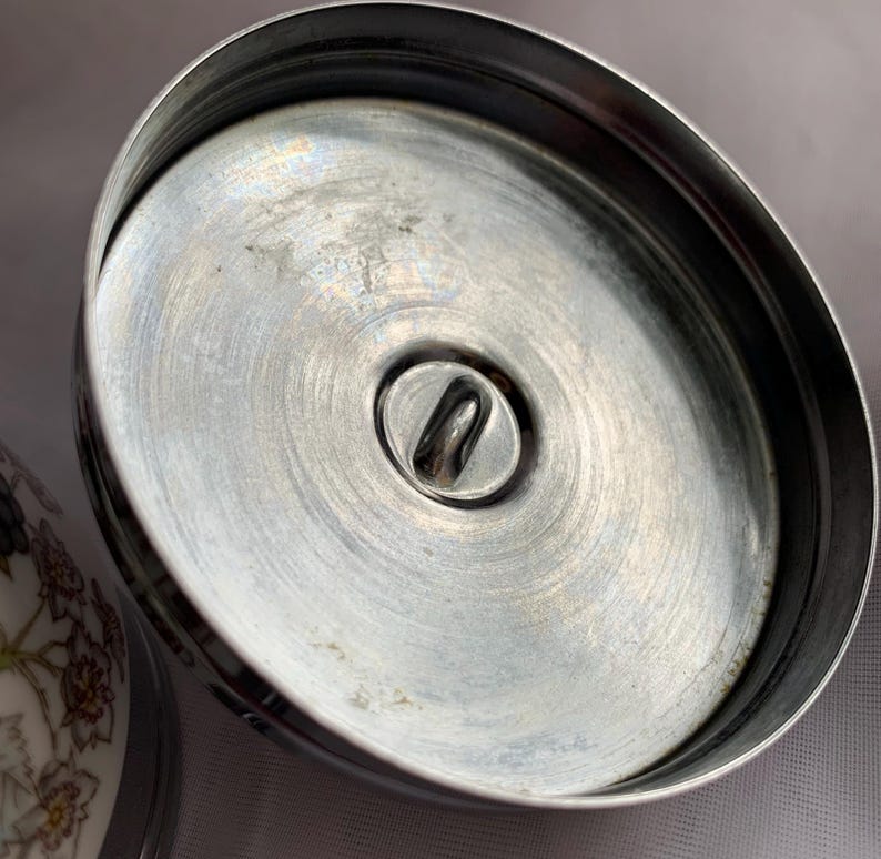 K&ouml;nnte beinhalten: Nahaufnahme der Unterseite eines silbernen Deckels mit einer kleinen Metallschlaufe in der Mitte.