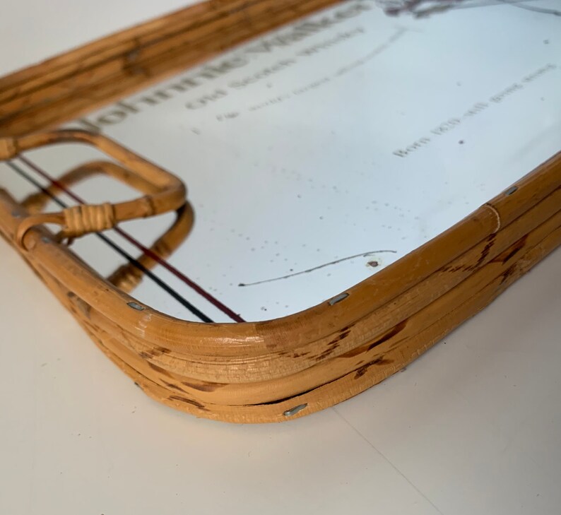 May include: A rectangular bamboo serving tray with a mirrored surface. The tray has a handle on one side and features the text "Johnnie Walker Old Scotch Whisky". The tray is a light brown color.