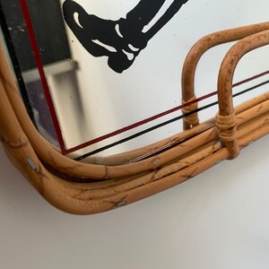 May include: A vintage rectangular rattan tray with a mirrored surface. The mirror features a black and white graphic of a leg and foot, with red and black lines. The tray has a curved handle.