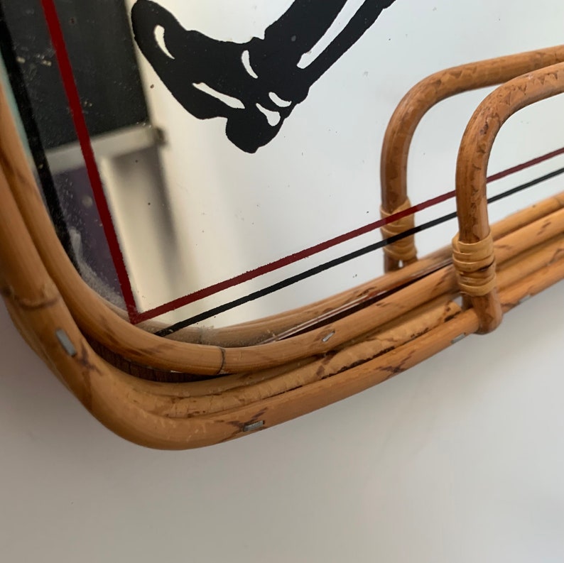May include: A vintage rectangular rattan tray with a mirrored surface. The mirror features a black and white graphic of a leg and foot, with red and black lines. The tray has a curved handle.