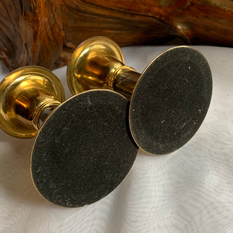 Op de afbeelding: Een paar gouden metalen kaarsenstandaards met zwarte viltpads aan de onderkant.
