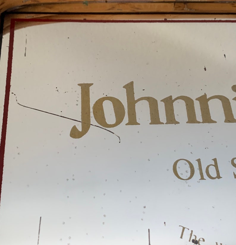 May include: A vintage sign with the name "Johnnie" in gold lettering. The sign has a white background with a red border and a wooden frame. The words "Old S" are also visible.