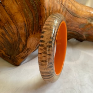 May include: A wooden bangle with a clear resin coating and a bright orange interior. The wood has a natural brown and black pattern.