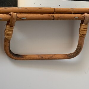 May include: Close-up of a bamboo mirror with a curved handle. The handle is made of bent bamboo and wrapped with woven material at the joints. The mirror frame is made of bamboo and secured with small metal staples.