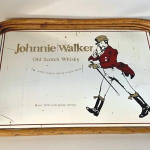 May include: Vintage Johnnie Walker Old Scotch Whisky serving tray. The tray features the brand's logo and a walking gentleman illustration in red, black, and white. The text "Born 1820-still going strong" is also visible.