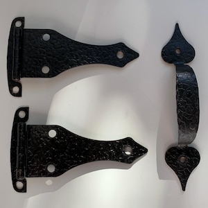 May include: Two black metal hinges with a decorative pointed design and a black metal door handle with a pointed design.