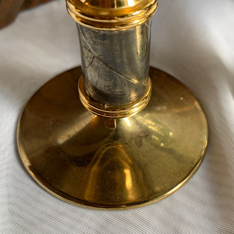 Op de afbeelding: Een gouden kandelaar met een zilveren voet. De voet heeft een getextureerd ontwerp en is omgeven door een gouden band.